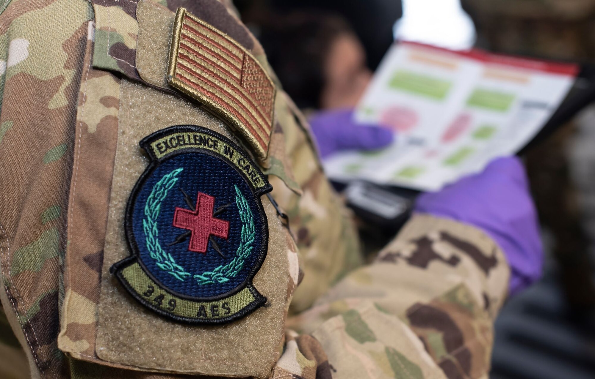The sleeve of a military person's combat uniform has the squadron patch of the 349th Aeromedical Evacuation Squadron on it. Its motto, "Excellence in Care," is emblazoned at the top.