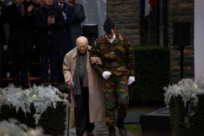 Man walks arm in arm with a service member during a memorial commemorating the 75th anniversary of the Battle of the Bulge.
