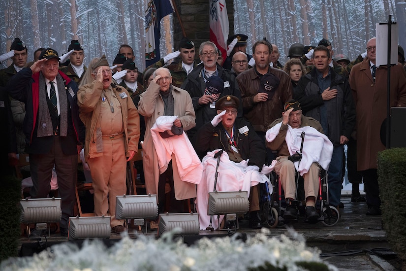 A group of men salute and sing at a memorial.