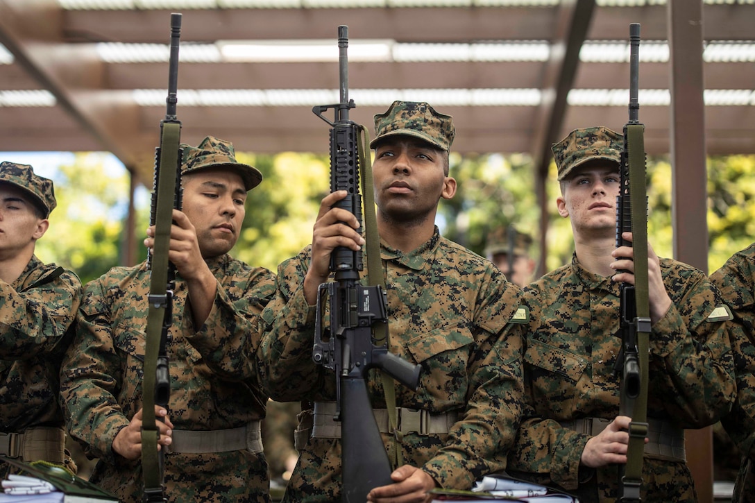 Marines Corps recruits hold up rifles.