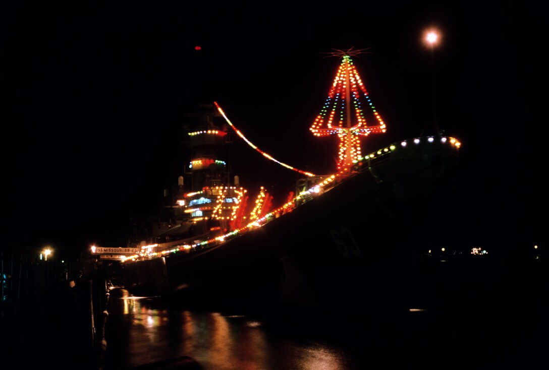 Lights adorn a moored ship at night.