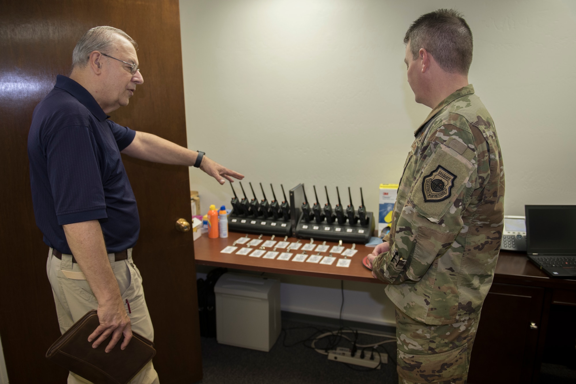 Sal Pampinella, left, International Treaty Compliance Office staff member, shows Col. Jeffrey Nelson, right, 60th Air Mobility Wing commander, the walkie-talkies and security badges they use when they escort international visitors Dec. 13, 2019, at Travis Air Force Base, California. Pampinella manages and directs all activities that involve foreign visitors. Nelson toured the International Treaty Compliance Office as part of the Leadership Rounds, a program that allows base leadership to connect with personnel and gain a more in-depth understanding of each section on base. (U.S. Air Force photo by Airman 1st Class Cameron Otte)