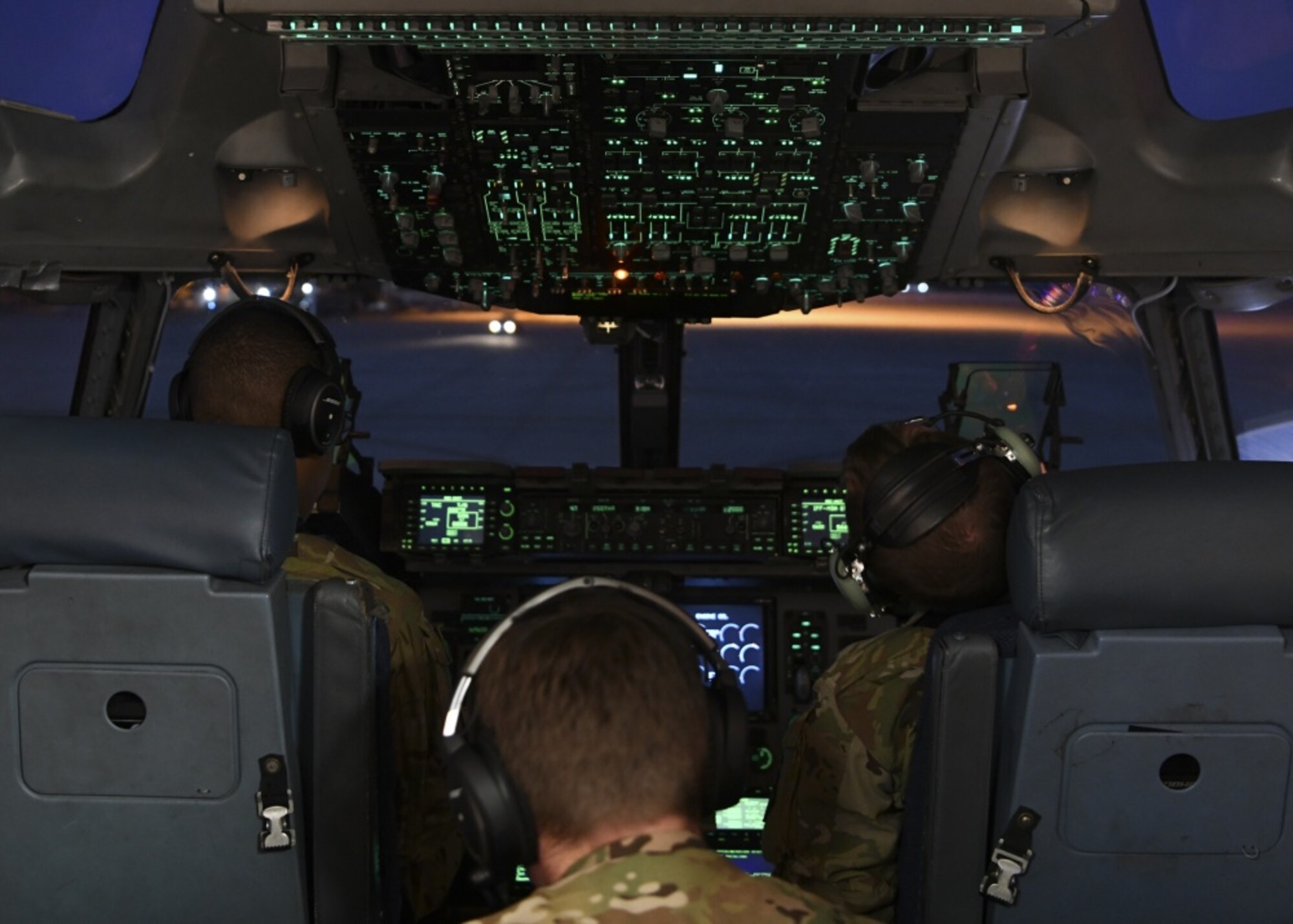 Three people sit in the cockpit of an aircraft.