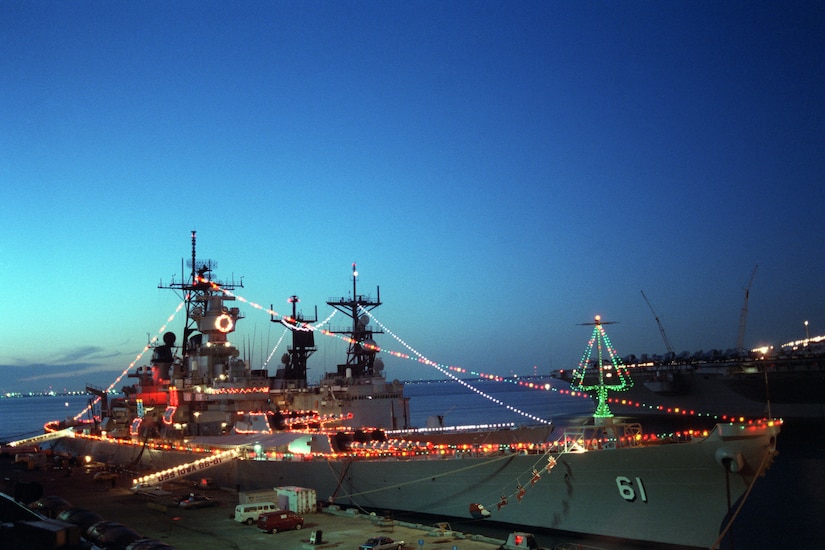 Two lighted ships sit at a pier.