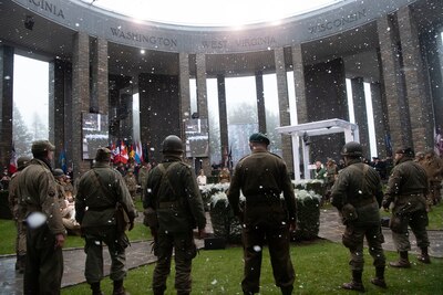 World War II reenactors in period uniforms stand at a ceremony with simulated snow falling.