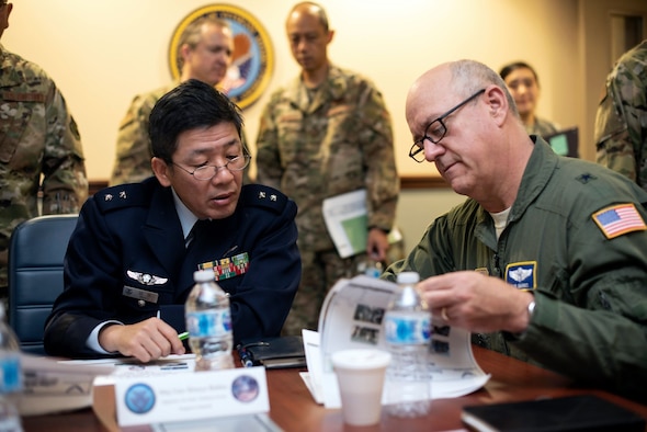 Gen. Shinya Bekku and Gen. Robert Marks pore over a pamphlet of documents. Various other military members look on.