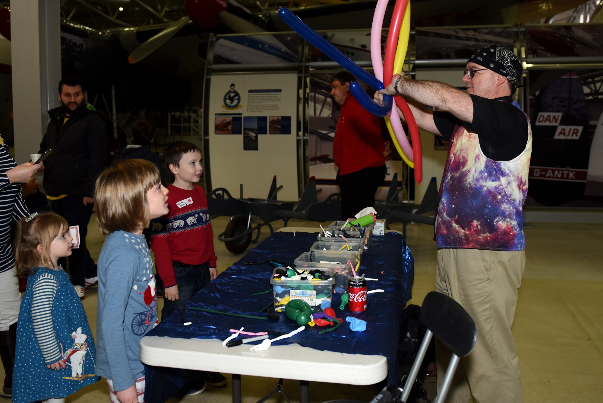 A balloon artist crafts a balloon animal for children at the Duxford Children’s Christmas Party at the Imperial War Museum, Cambridgeshire, England, Dec. 14, 2019. The event featured games, Morse code lessons, pilot displays, and a visit from Father Christmas himself. (U.S. Air Force photo by Airman 1st Class Rhonda Smith)