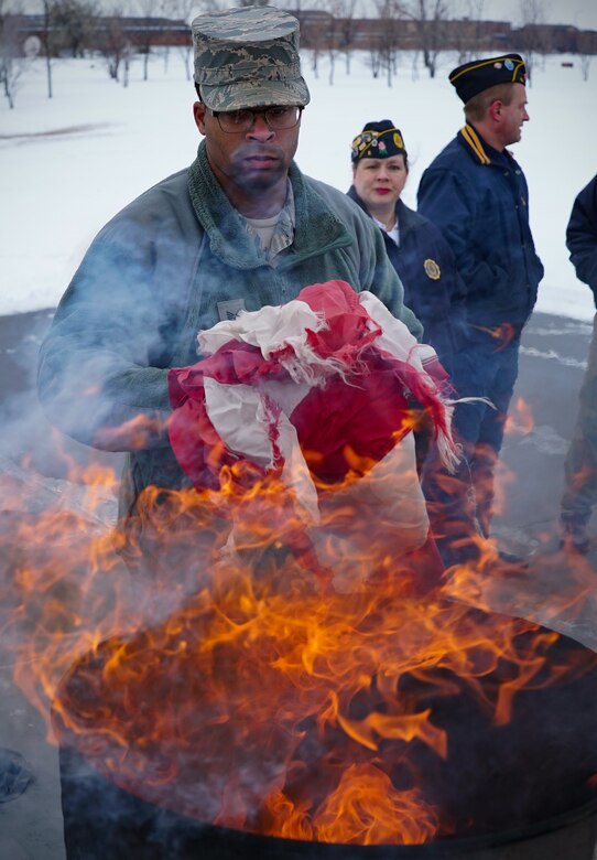 Staff Sgt. Alonzo Clark, installation honor guard program manager, steps forward to place an unserviceable U.S. flag into the flames of a ceremonial flag burn Dec. 7, 2019, on Grand Forks Air Force Base, North Dakota. Ceremonial flag burns such as the one Clark participated in are meant to honorably destroy U.S. flags that have become worn, faded or otherwise unserviceable during the span of their lifetime. (U.S. Air Force photo by Senior Airman Elora J. Martinez)