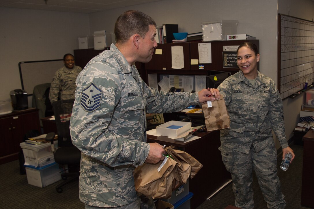 U.S. Air Force Master Sgt. Ryan Trandell, 633rd Comptroller Squadron first sergeant, hands a bag of cookies to Airman 1st Class Olivia McKinsey, 633rd Air Base Wing Judge Advocate military justice paralegal, at Joint Base Langley-Eustis, Virginia, Dec. 13, 2019.