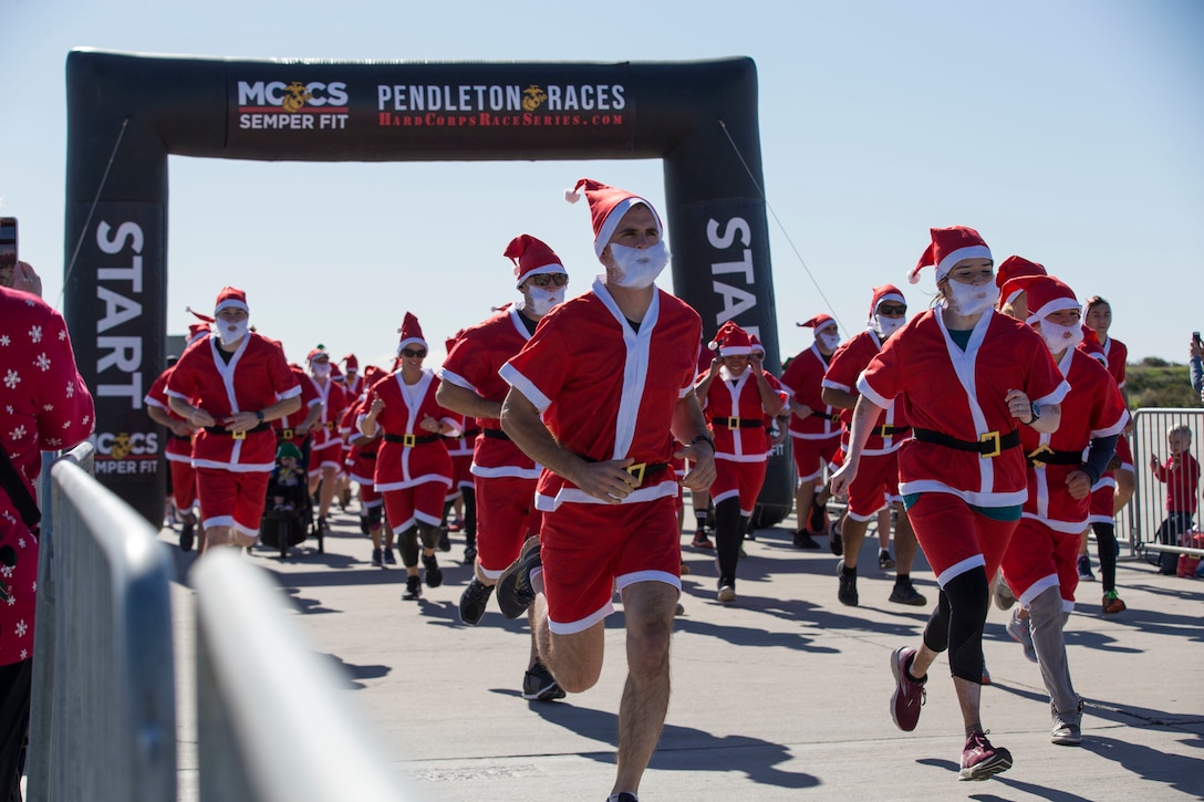 Men and women dressed in Santa Claus suits run down a street.