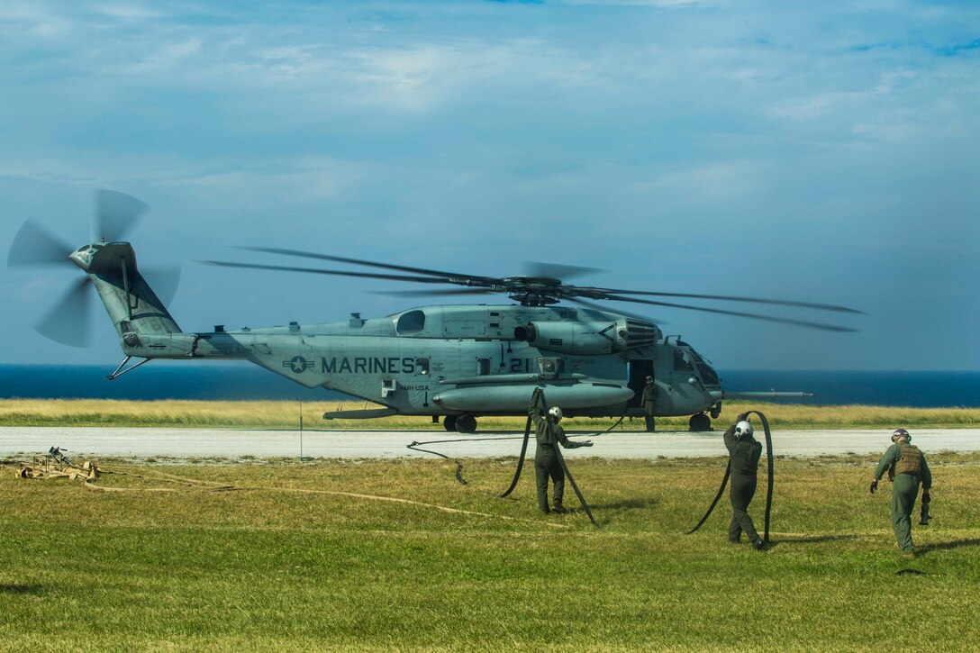 Three Marines hold a hose with a helicopter parked in front.