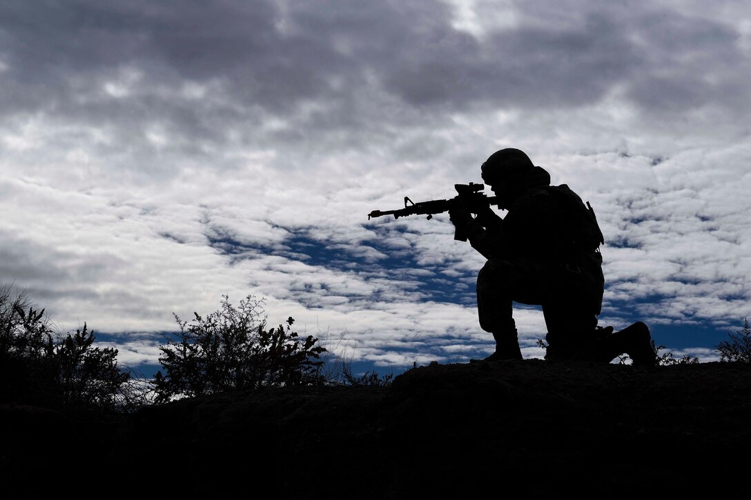 A silhouette of an airman kneeling on the ground pointing a weapon.