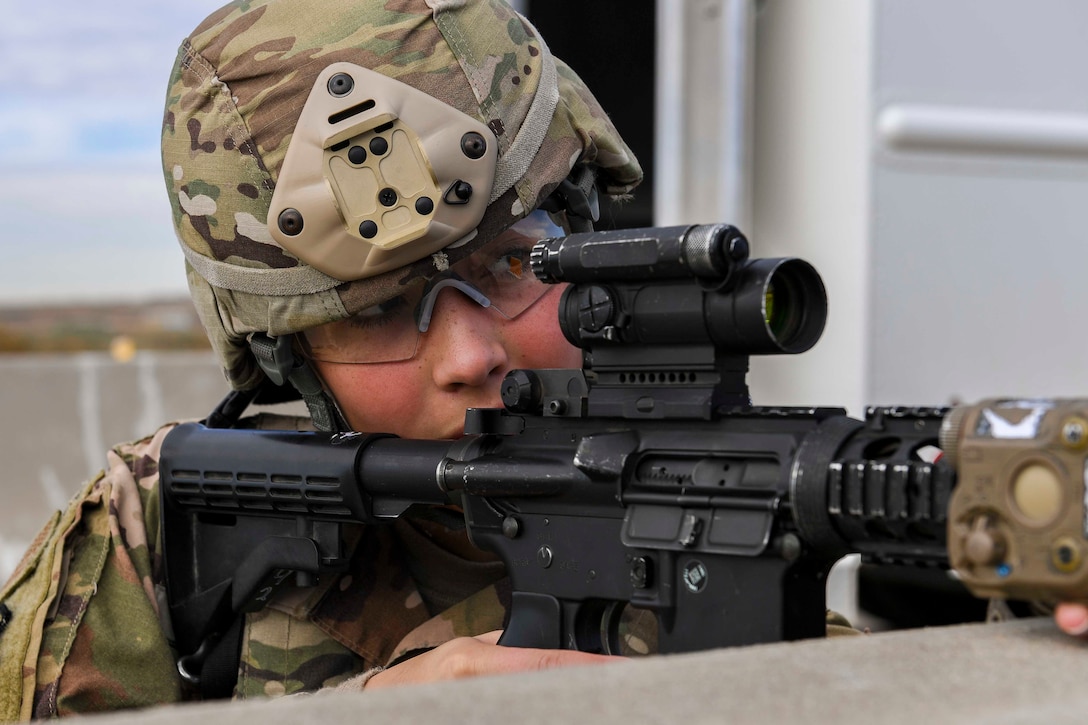 An airman looks through a view finder on a rifle.