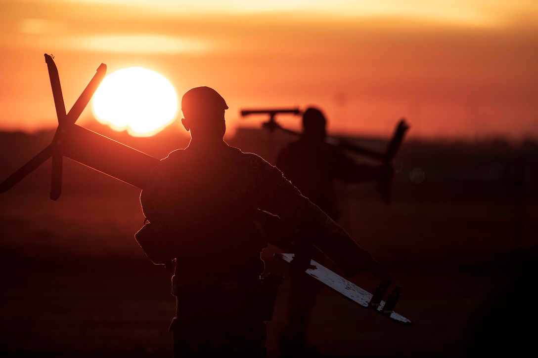 Two airmen carry shooting targets at dusk.