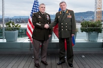 U.S. and Russian generals stand in front of their respective nations’ flags and shake hands.