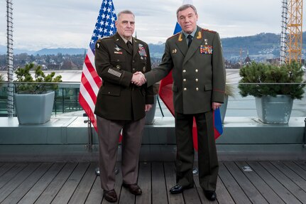 U.S. and Russian generals stand in front of their respective nations’ flags and shake hands.