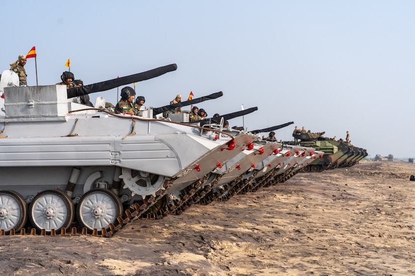 A handful of military tanks are lined up on the sand.