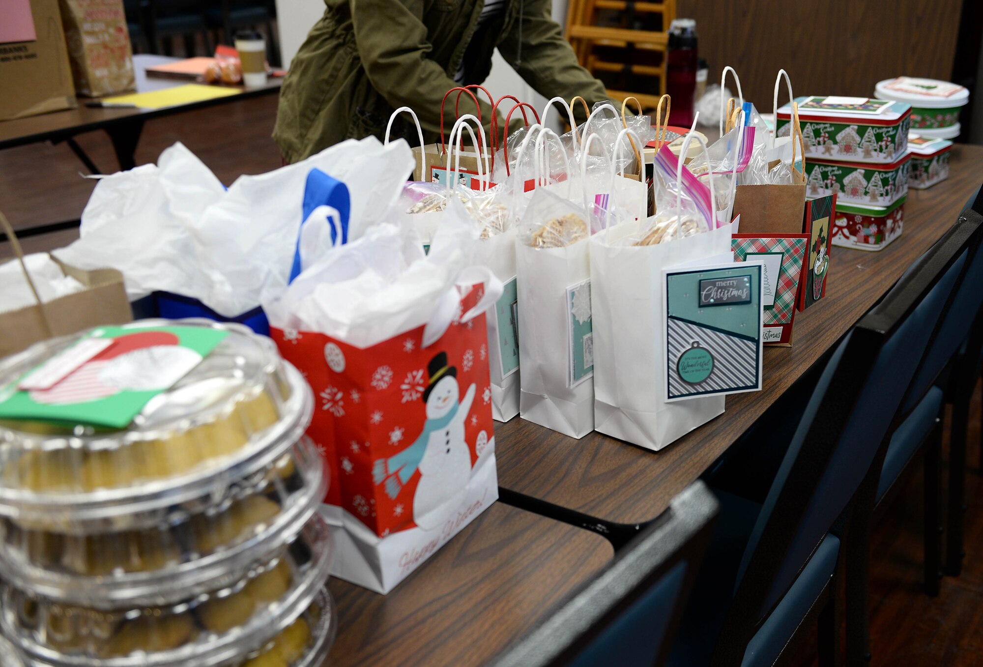 Bags and tins of cookies lay stacked on a table in preparation for the Columbus Spouses Club Cookie Drive at the BLAZE Chapel Annex Dec. 16, 2019, on Columbus Air Force Base, Miss. Volunteers from across the base and community came together to bake, package and deliver nearly 700 dozen cookies to Airmen across the base. (U.S. Air Force photo by Airman 1st Class Hannah Bean)