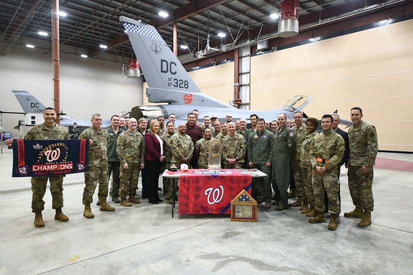 Airmen from the 113th Wing, District of Columbia Air National Guard, pose for a group photo with Washington Nationals staff and the World Series trophy, during a display event at Joint Base Andrews, Md., Dec. 17, 2019. The 113th Wing presented Ryan Zimmerman, Washington Nationals first baseman, with a certificate and flag that was flown by the unit over the nation’s capital. (U.S. Air Force photo by Airman 1st Class Spencer Slocum)