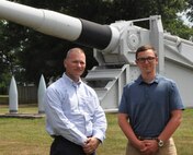 IMAGE: DAHLGREN, Va. (July 12, 2019) – U.S. Naval Academy Midshipman Jonathon Copley and his mentor, Mike Burchik, a Naval Surface Warfare Center Dahlgren Division (NSWCDD) scientist, are pictured in front of a U.S. Navy 16-inch battleship gun on the parade field near NSWCDD headquarters during Copley’s summer internship. While assigned to the Submarine Launched Ballistic Missile Program (SLBM), Copley worked with a team that supported developers who wrote code for the SLBM Fire Control System. “I was astonished to see how many people were on the base working hard to keep our Navy on the cutting edge while maintaining the technology gap with our adversaries,” said Copley. “They are working day in and day out to enhance the Navy's warfighting ability. It made me proud to know I will be joining a fighting force with such superb people behind it.” (U.S. Navy photo/Released)