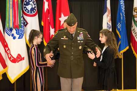 Two young girls stand to each side of male Soldier in green Army uniform
