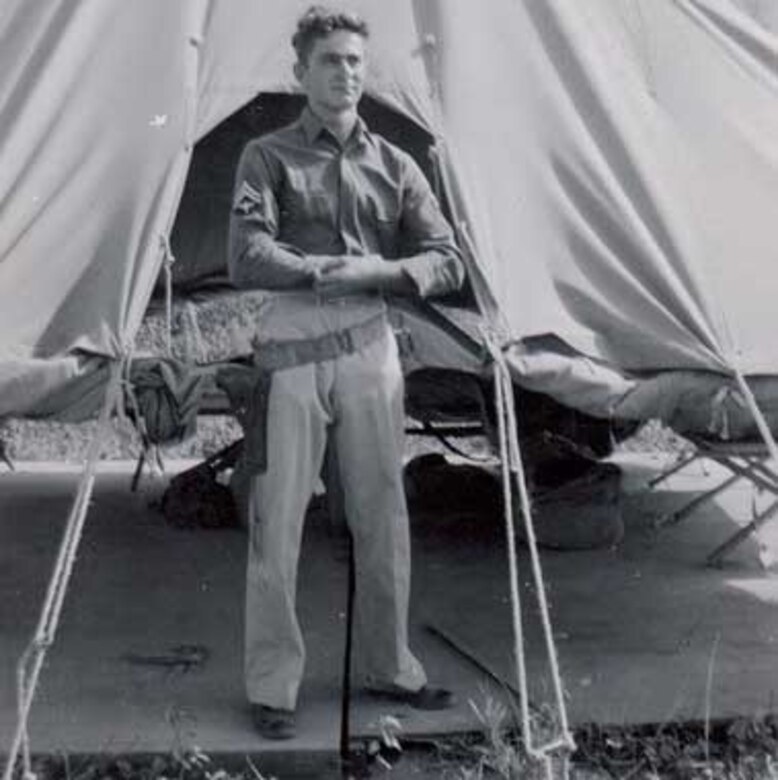 A  man poses next to a tent.