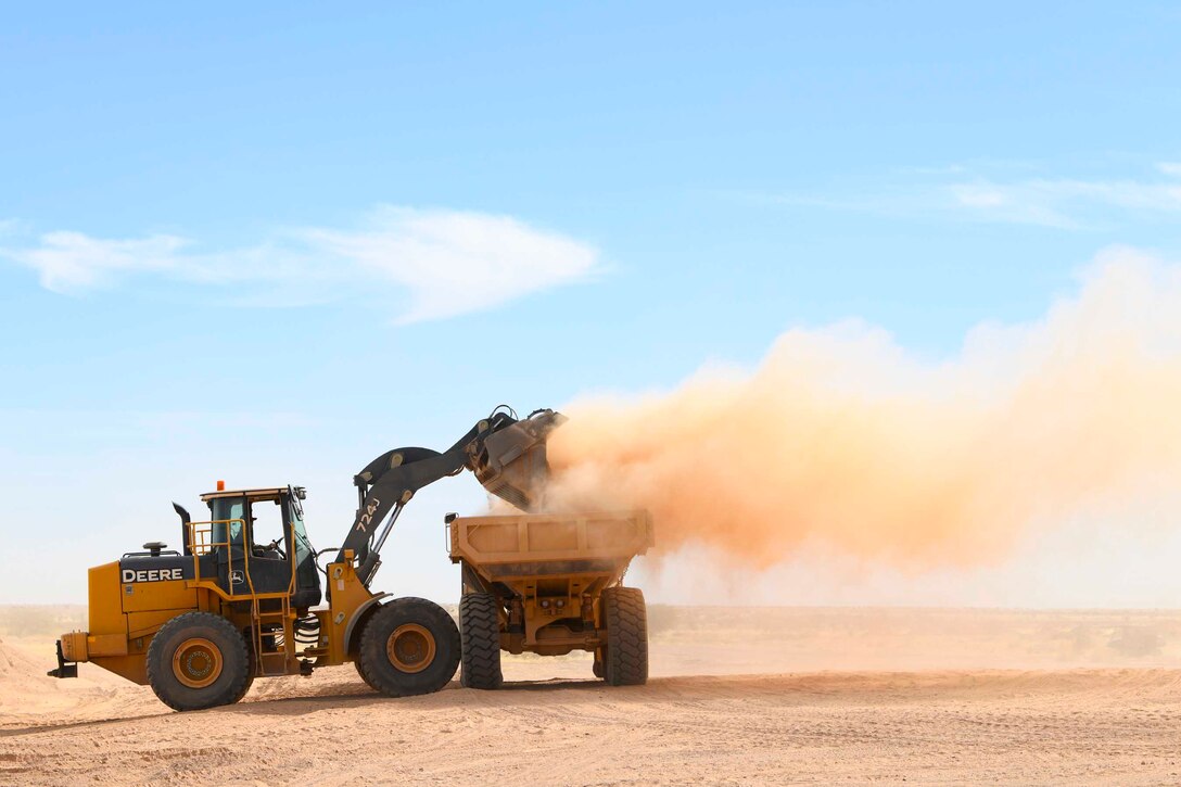 A construction vehicle moves dirt into a dump truck.