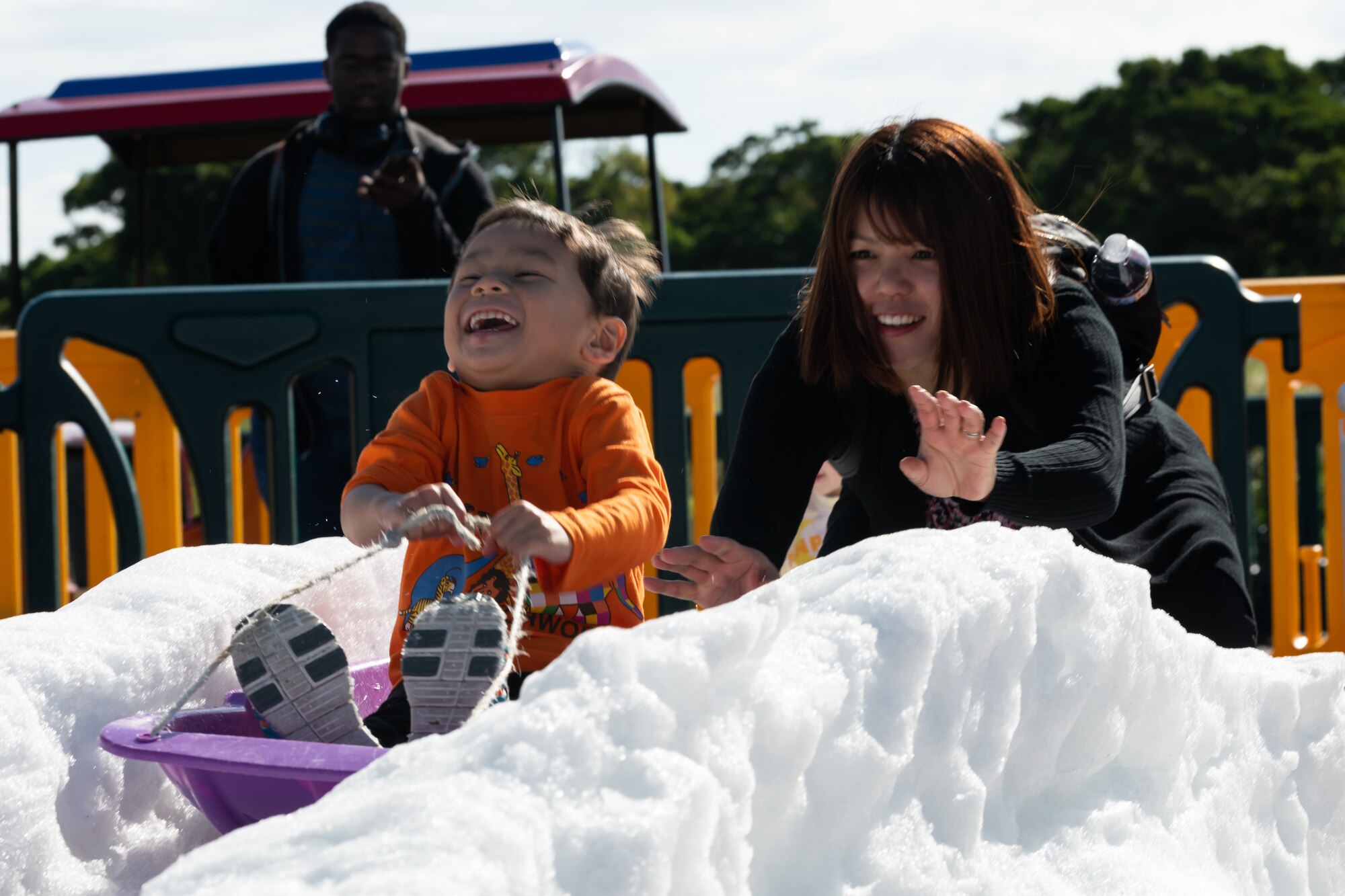 A woman pushes a child on a snow sled during the 18th Wing Tinsel Town event at Kadena Air Base, Japan, Dec. 14, 2019. Other events and games included a rock climbing wall, food trucks, and more. (U.S. Air Force photo by Senior Airman Matthew Seefeldt)