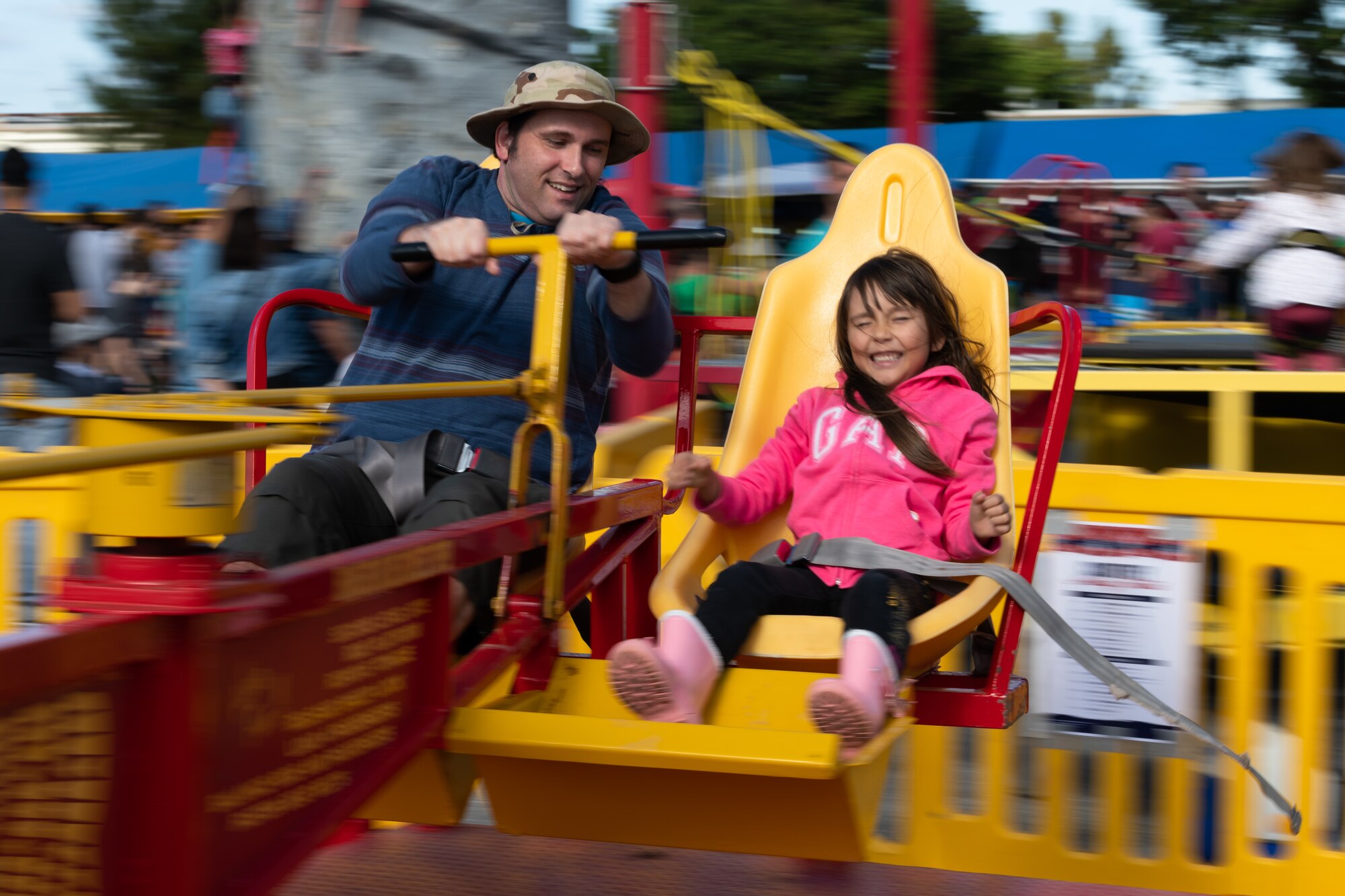 A man and girl ride an amusement park ride during the 18th Wing Tinsel Town event at Kadena Air Base, Japan, Dec. 14, 2019. Other events and games included a rock climbing wall, food trucks, and more. (U.S. Air Force photo by Senior Airman Matthew Seefeldt)