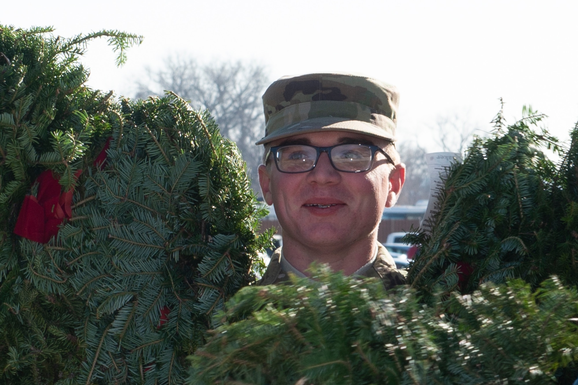 A Team Offutt volunteer smiles as he carries wreaths to the base cemetery, at Offutt Air Force Base, Neb., Dec. 11, 2019. Volunteers helped unload 86 boxes of wreaths that were delivered by a semi truck in preparation for a Wreaths Across America ceremony.