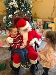 A boy sits on Santa's lap while a girl stands in front.