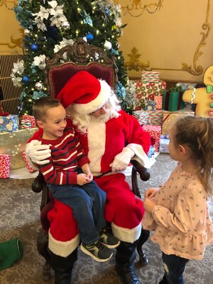 A boy sits on Santa's lap while a girl stands in front.