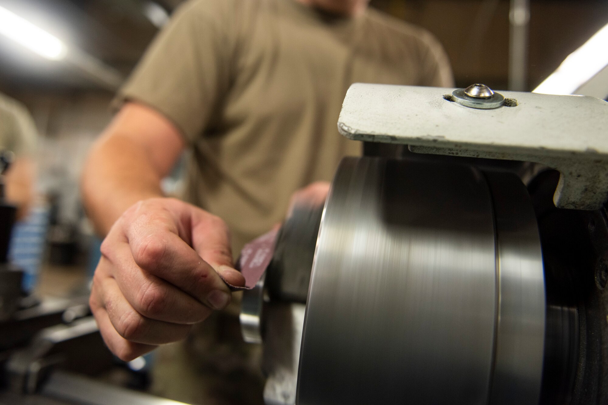 A photo of an Airman using sandpaper to smooth a bushing while it's rotating.