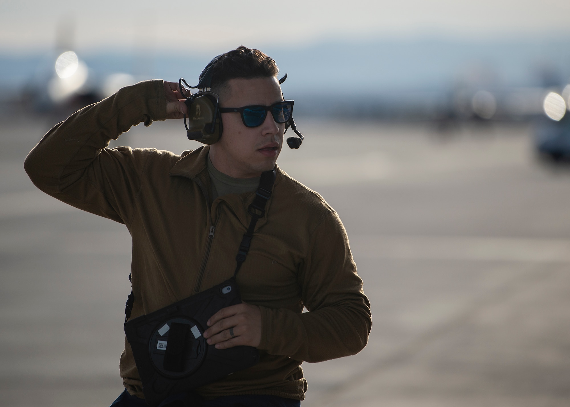 An Airman adjusts his headset while holding a tablet.