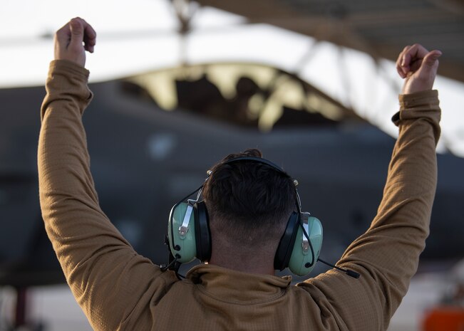 An Airman lifts his hands above his head to signal a pilot in a F-35A Lightning II fighter jet.
