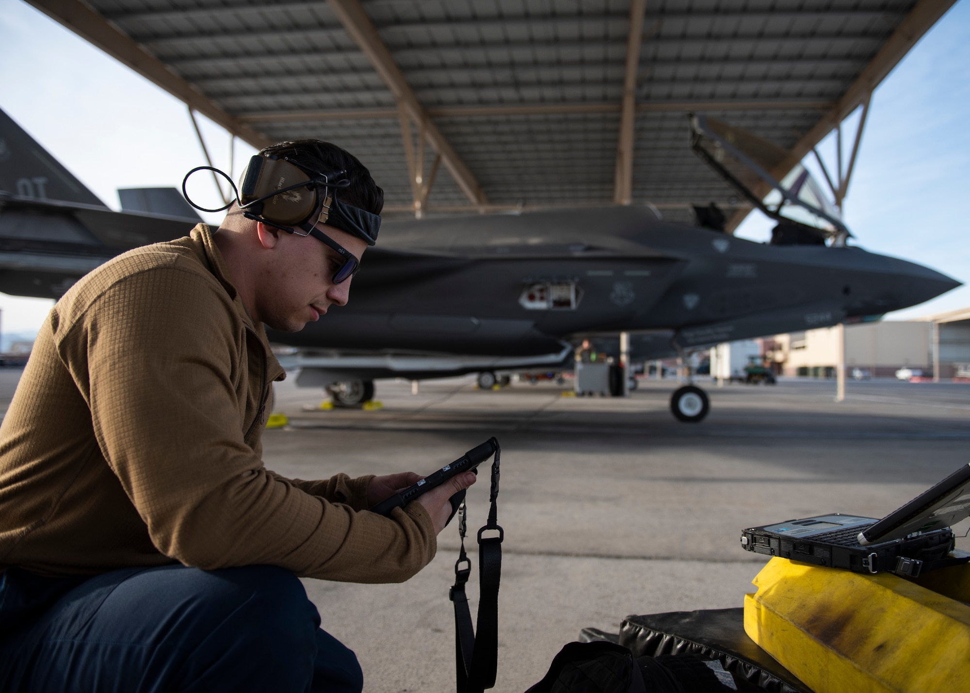 An Airman holds a tablet with an F-35A Lightning II fighter jet in the background.