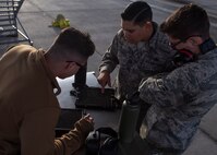 Three Airmen huddle around a tool box with a tablet laying on top of it.