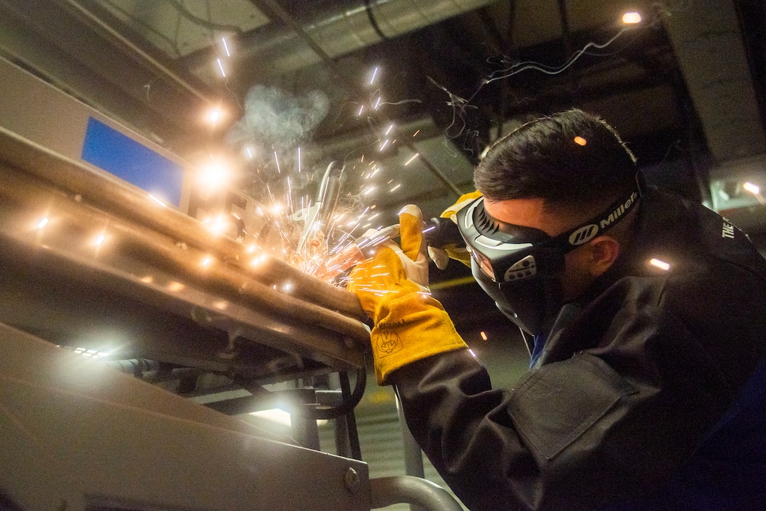 A photo of an airman welding while sparks fly.
