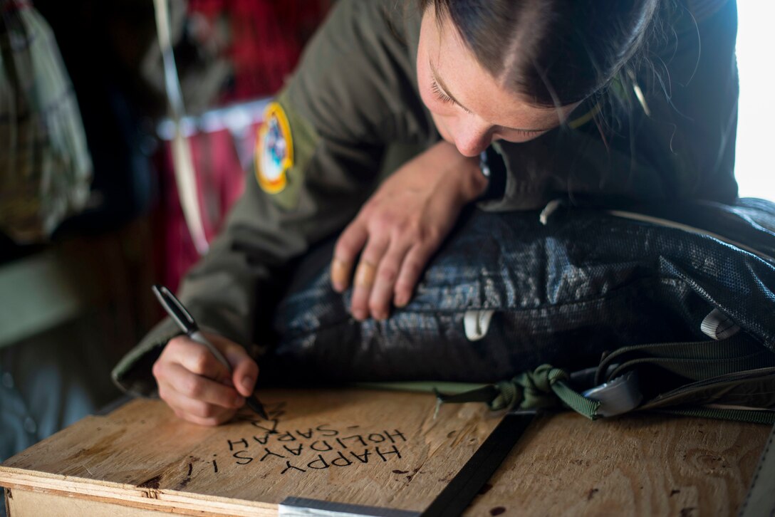 An airman writes a message on a large box.