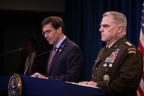 A civilian speaks and a military officer looks forward while both men stand behind podiums.