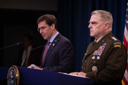 A civilian speaks and a military officer looks forward while both men stand behind podiums.