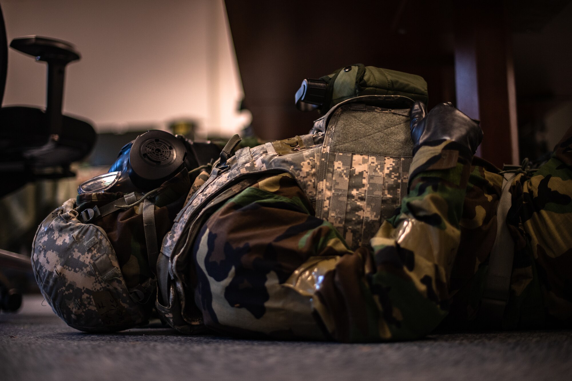 An Airman dressed in Mission-Oriented Protective Posture gear takes cover under a desk