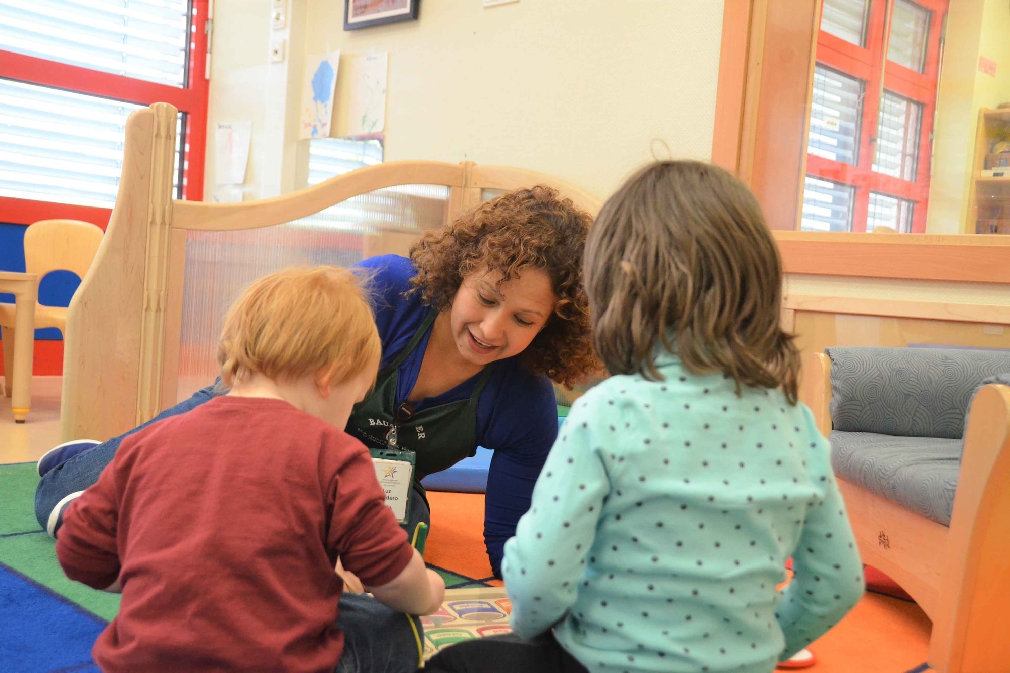 A woman sits on the floor and plays with two children.