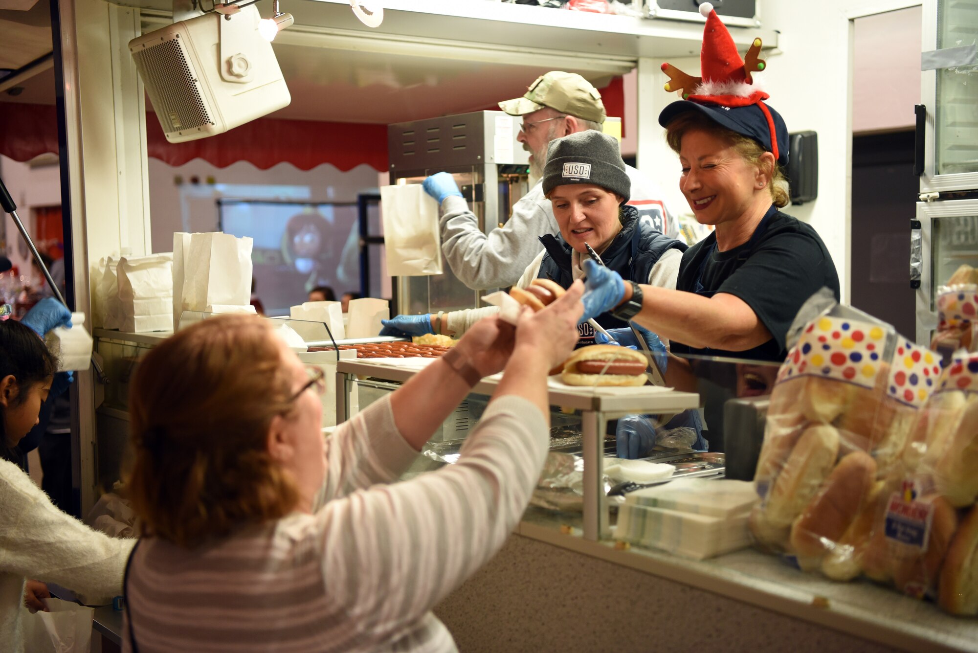 United Service Organizations volunteers serve hot dogs to families during the Rudolph the Red Nosed Herc event at Ramstein Air Base,Germany, Dec. 20, 2019.