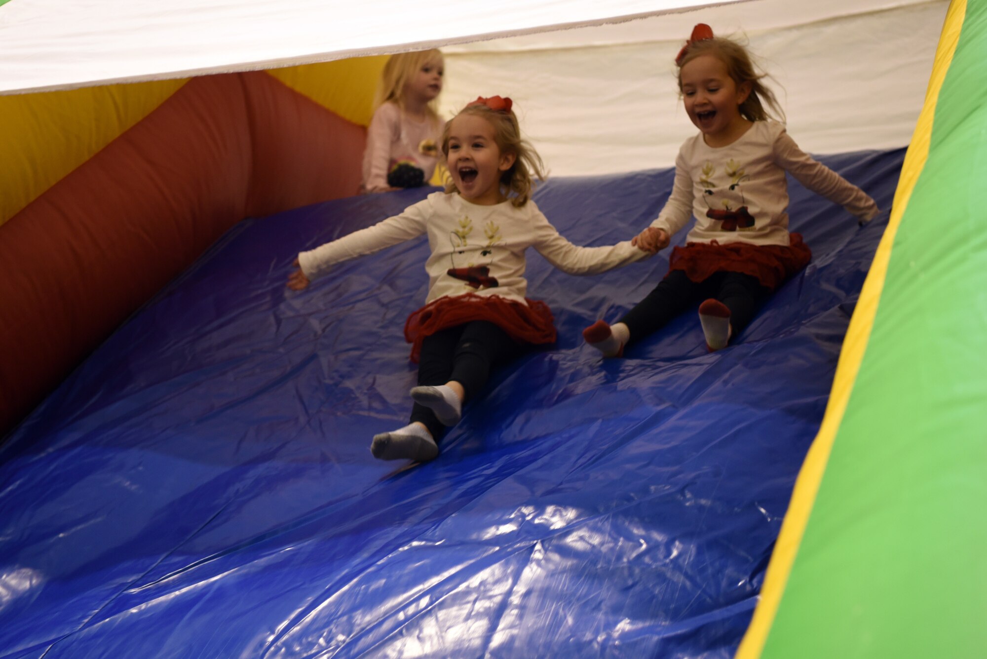 Lillian and Rylee, daughters of U.S. Air Force Maj. Casey Brown, 86th Airlift Wing, Wing Plans and Programs action officer and pilot, hold hands as they slide down an inflatable slide during the Rudolph the Red Nosed Herc event at Ramstein Air Base, Germany, Dec. 20, 2019.