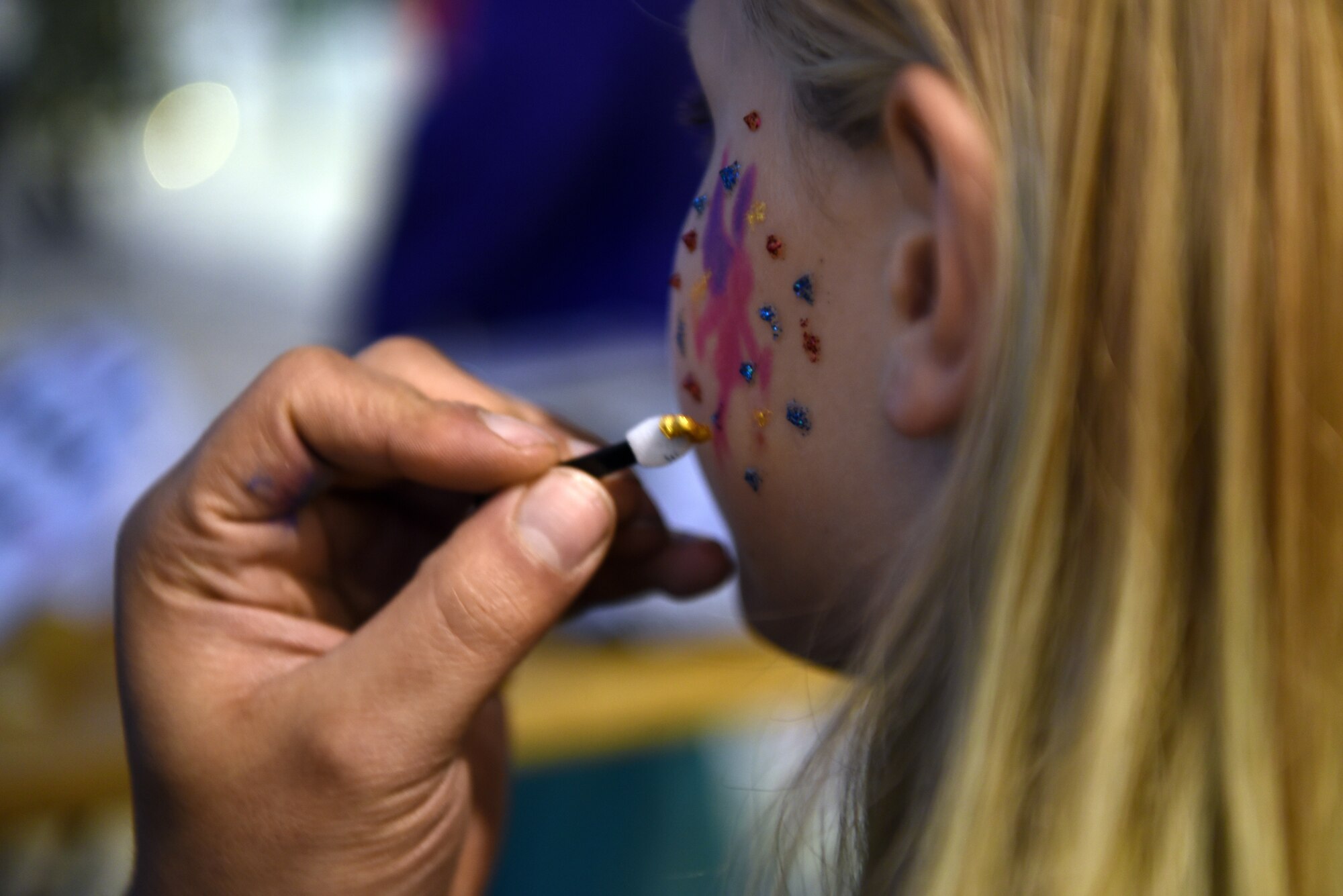 U.S. Air Force Senior Airman Patrick Strader, 86th Maintenance Squadron aerospace propulsion journeyman, paints the faces of children attending the Rudolph the Red Nosed Herc event at Ramstein Air Base, Germany, Dec. 20, 2019.