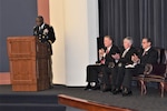 Army Lt. Gen. Darrell K. Williams stands at a lectern on stage with three Army Command and General Staff School officials seated behind him applauding