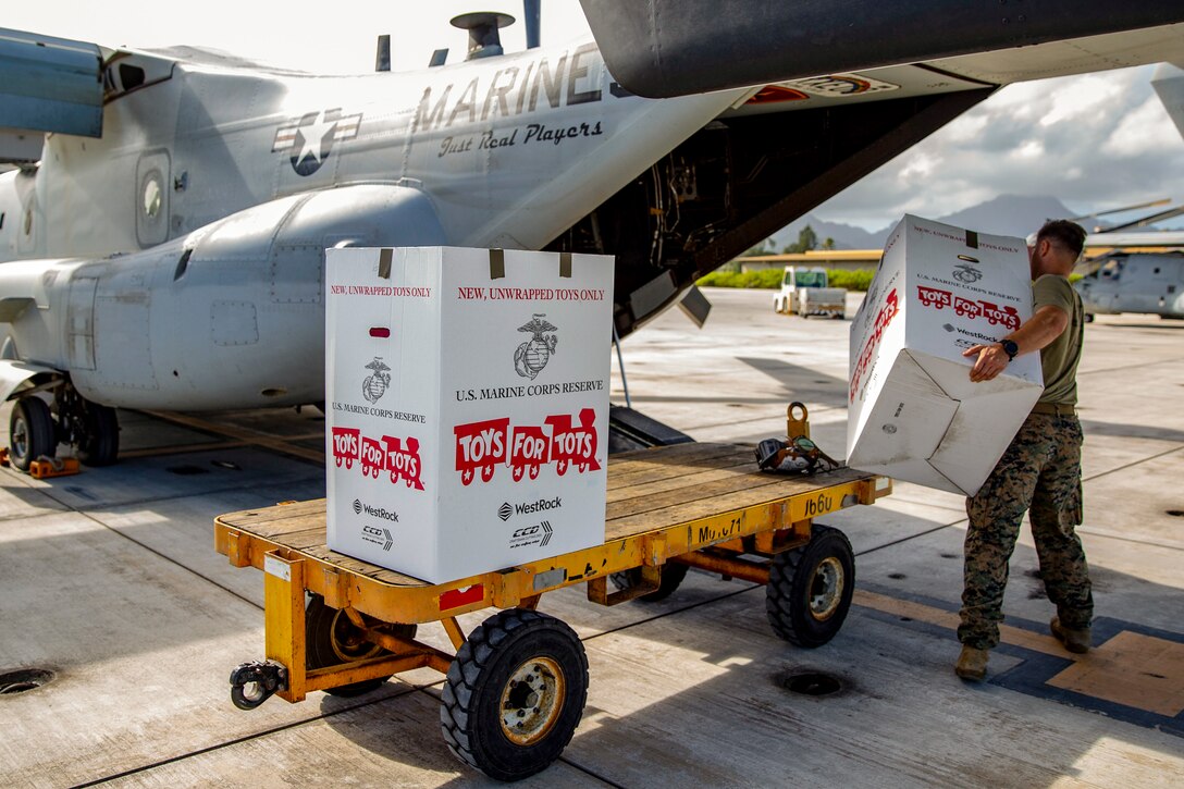 A Marine loads Toys for Tots boxes into the back of an Osprey aircraft on a flightline.