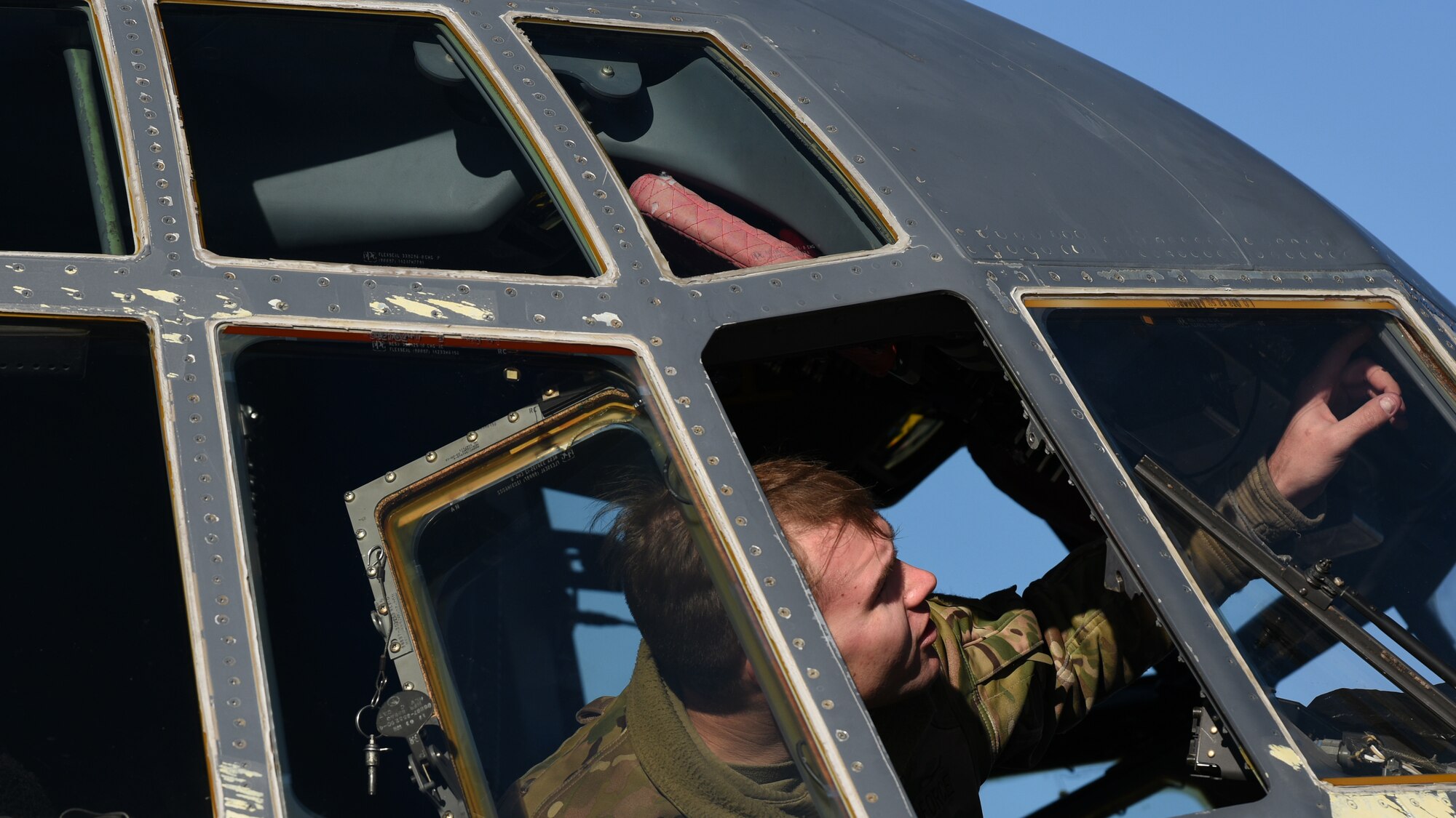 Photo of an Airman performing maintenance on a carrier aircraft's cockpit window