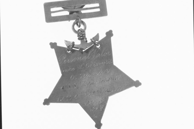 The backside of a Medal of Honor attached to a clasp. Illegible engraving is on the medal.